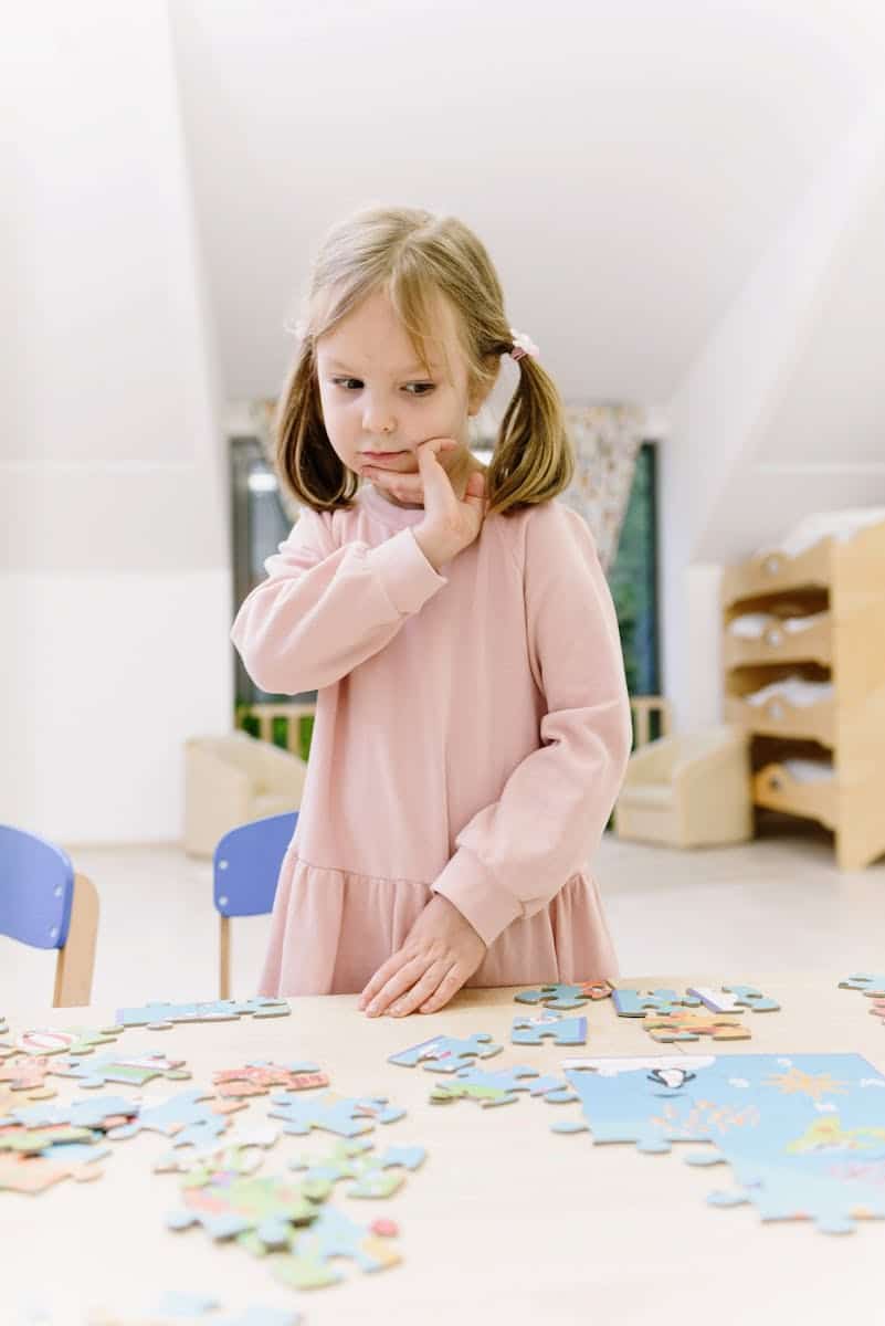 A young girl contemplating while assembling a puzzle in a modern indoor setting.
